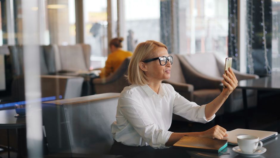 Empresária sorridente fazendo uma videochamada em um café moderno, aproveitando uma pausa para o café.
