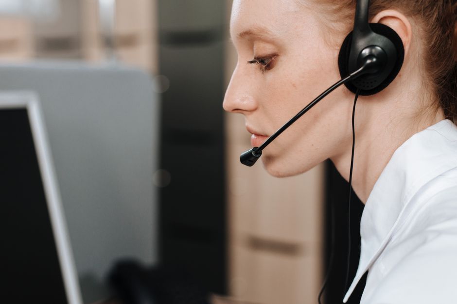 Foto em close de uma agente de call center feminina usando um fone de ouvido enquanto trabalha em sua mesa.
