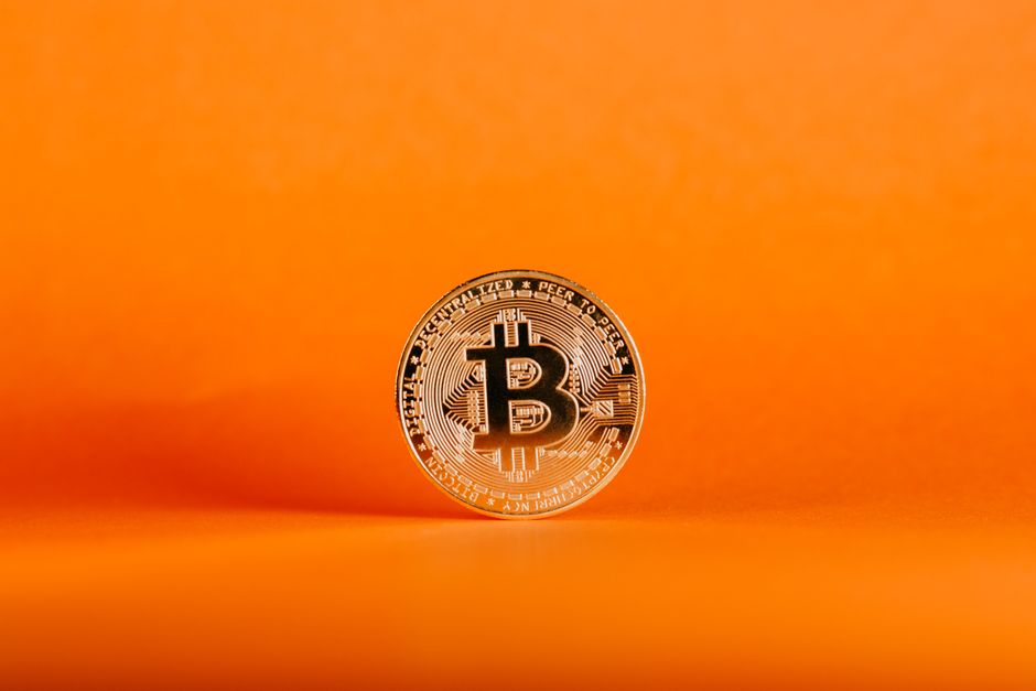 Close-up de uma moeda Bitcoin em um fundo laranja, simbolizando criptomoeda digital.