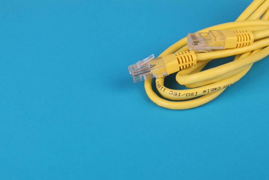 Close-up de um cabo Ethernet amarelo com conectores sobre um fundo azul.