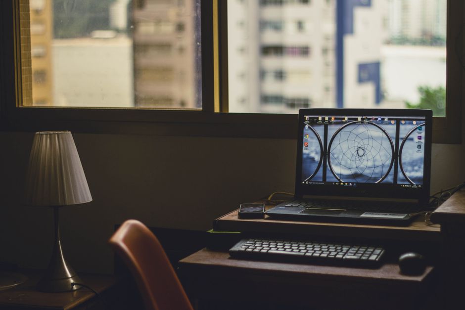 Um ambiente tranquilo de escritório em casa com um laptop, luminária e vista da cidade pela janela.