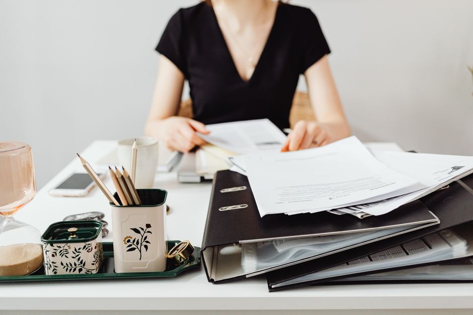 Uma mulher em uma mesa trabalhando com pastas e documentos, apresentando suprimentos de escritório essenciais.