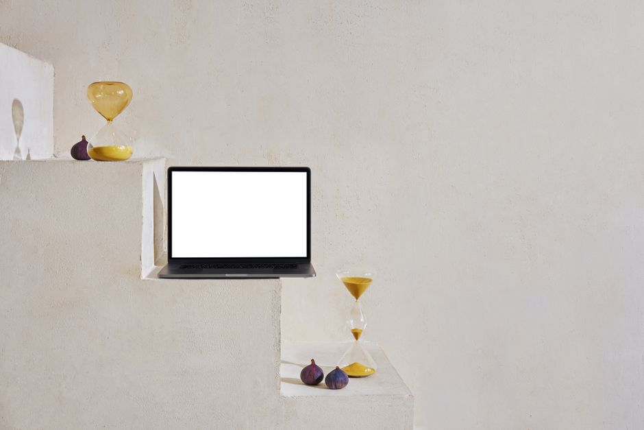 Uma cena minimalista com uma ampulheta, laptop e figos em uma escada.