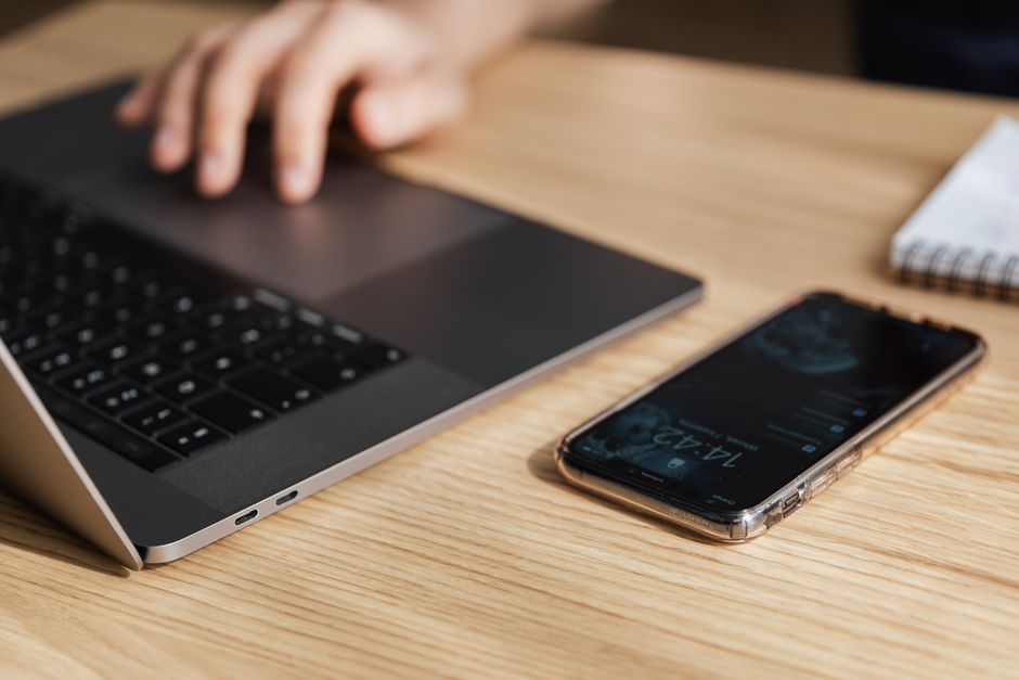 Uma mão em um laptop ao lado de um smartphone em uma mesa de madeira, simbolizando a vida moderna de trabalho.