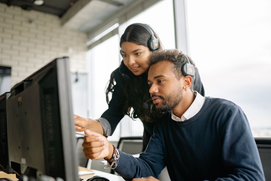 Dois funcionários de call center trabalhando juntos com headsets em um ambiente de escritório moderno.