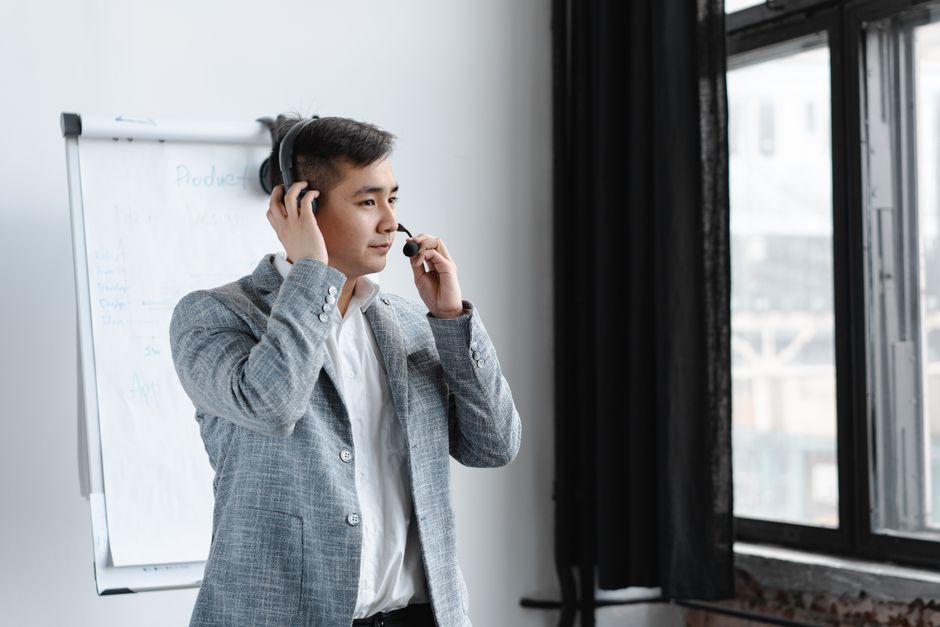 Agente de call center asiático usando um headset, atendendo ao serviço ao cliente em um escritório com vista para a janela.
